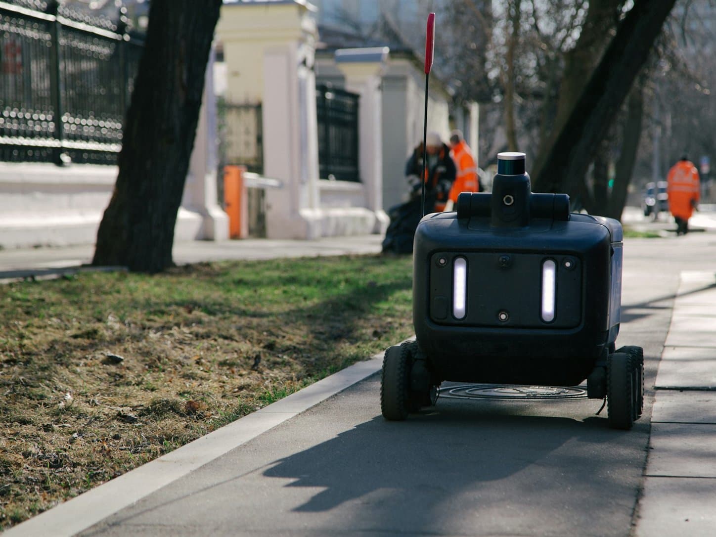 A six-wheeled unmanned ground vehicle carrying a rotating laser scanner, running a route along a paved path