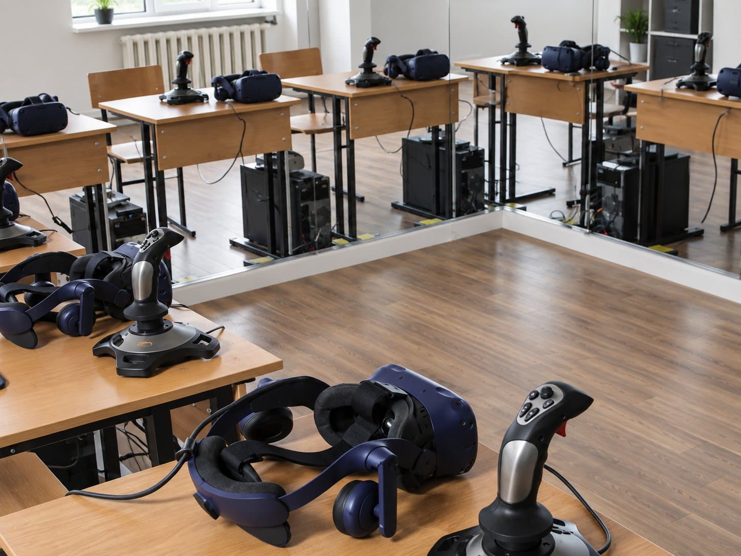 Training room of simulator stations, each with a VR headset and a flight-style control stick at the desk, tower PCs racked underneath